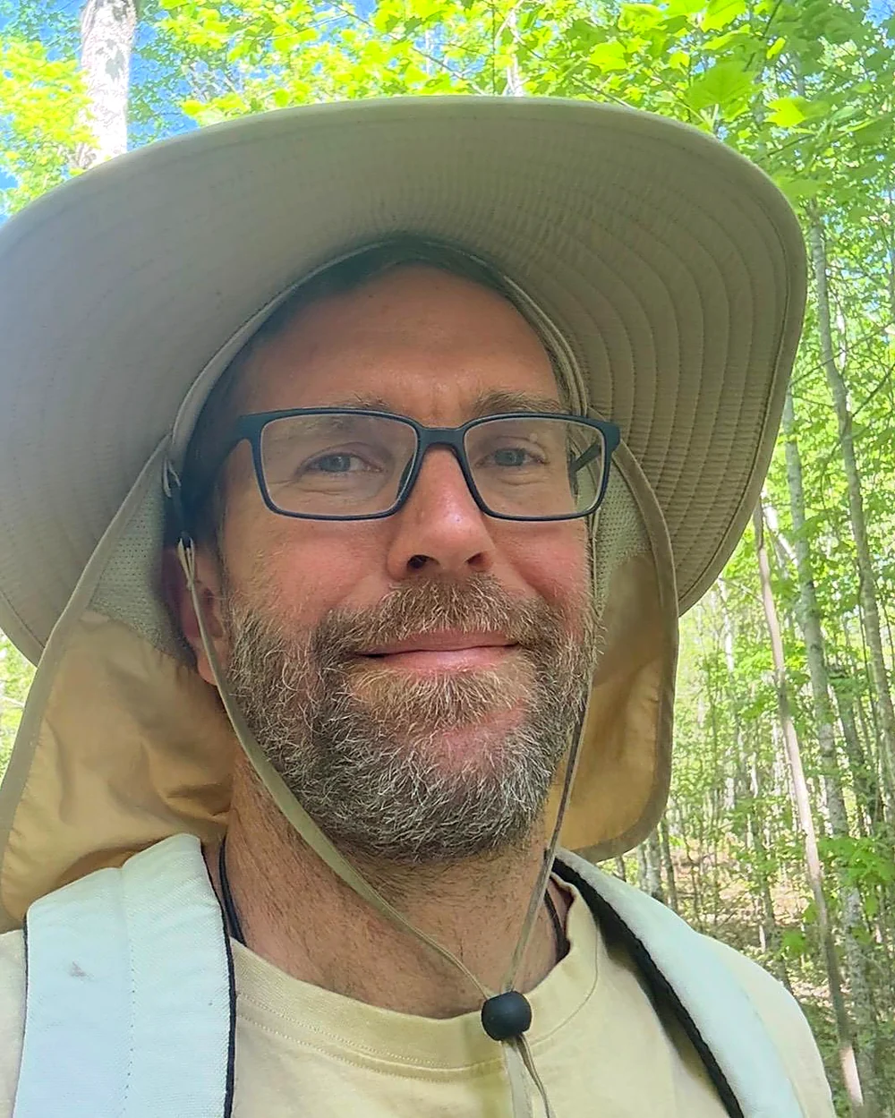 Matt Rogers, founder of A Tiny Getaway, wearing a wide-brimmed sun hat in a birch forest
