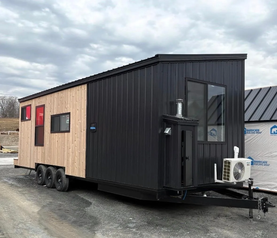 Tiny home clad in black steel and cedar sitting on a triple-axle trailer