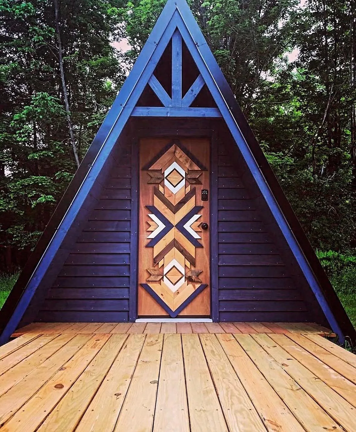 A-frame cabin with a carved geometric front door opening onto a timber deck
